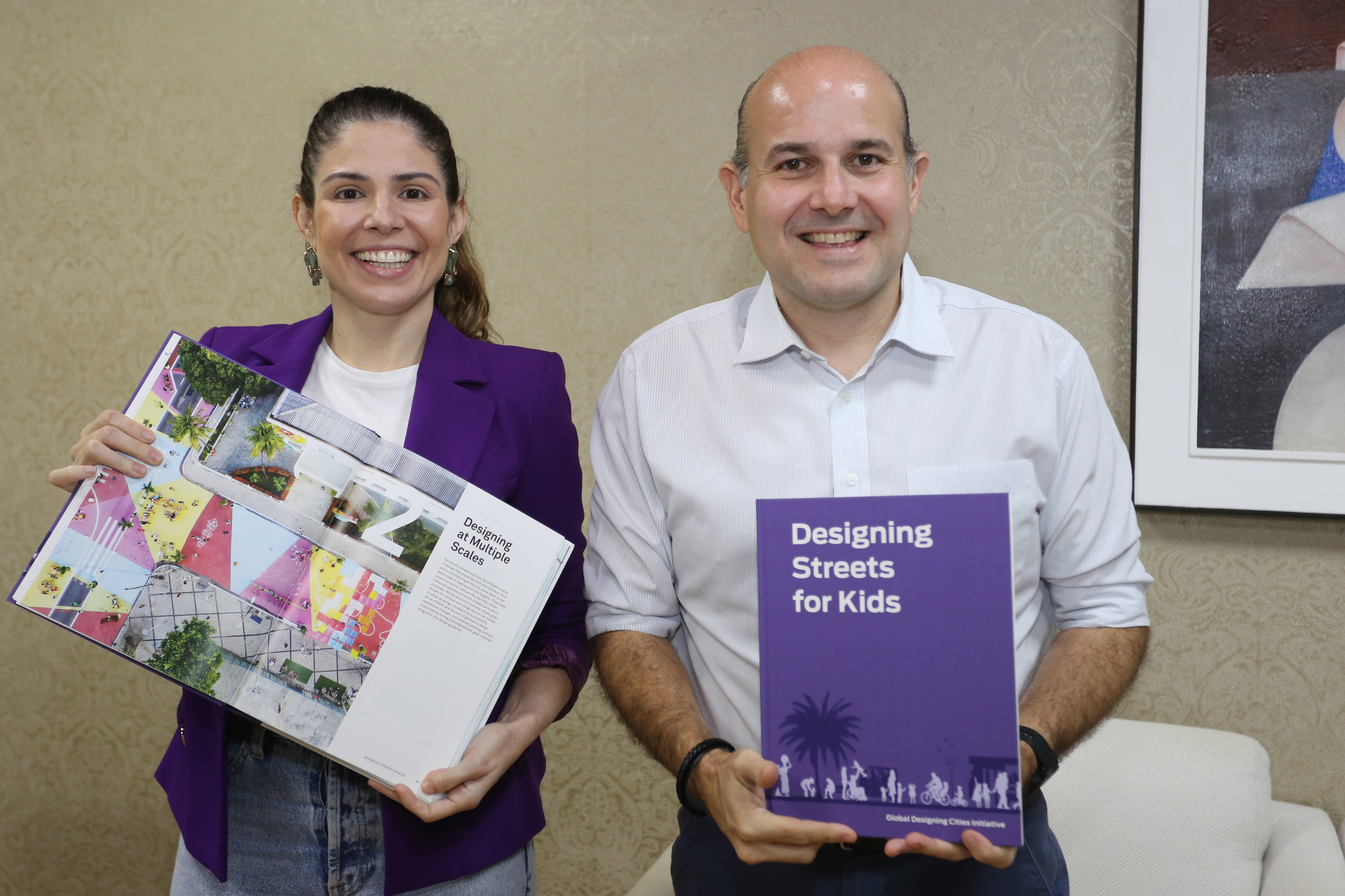 primeira-dama e prefeito lado a lado sorrindo para a foto segurando livros do projeto